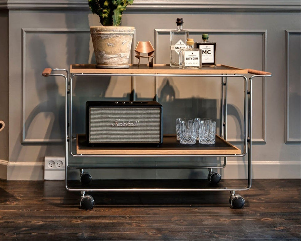 Chariot bar HB 128 par Horst Brüning, structure en acier chromé et plateaux en bois, design moderniste édité par Lange Production, présenté par Longitude Interior Design à Marseille. Accessoirisé